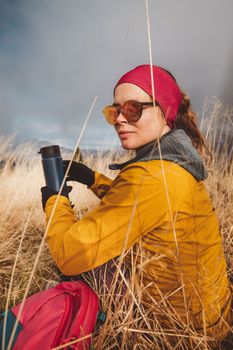 Waist up woman hiker looking away from the camera holding a blue thermo flask in her hands, hiking on a foggy autumn day,