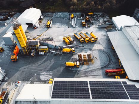 Aerial view in industrial area, directly above construction company, firm with lots of heavy machinery on the grounds, yellow trucks and other vehicles.