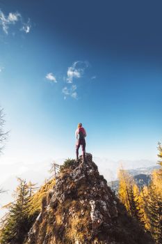 Scenic view of autumn mountain, European Alps, from a view point, where caucasian woman hiker is standing. Sun is shining high up in the mountains, a light mist in the valleys down bellow. Woman mountaineer enjoying the view of majestic Alps on a sunny autumn day.