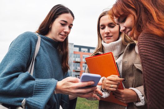 Group of three cheerful female collage students outside their dorm on a cold autumn day, walking on campus to get to their class.