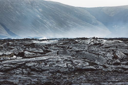 Geldingadalir active Volcano, errupting in 2021 - Fagradalsfjall and 2022 -Meradalir. Still hot lava rocks, steam comping up from the grounds. Dark grey, black volcanic rocks in Iceland. Dramatic view of lava rocks cold cloudy autumn day in Iceland.