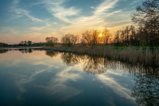 Sunset behind the trees over a calm lake, spring evening in eastern Poland