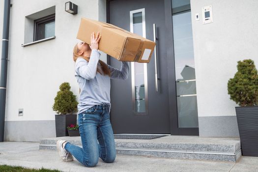 Thrilled caucasian woman kneeling down at the front door with a big cardboard box that just came in the mail. Woman receiving an exciting package.
