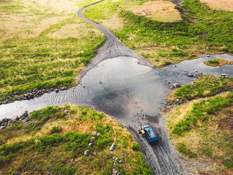 Remote dirt road somewhere in Iceland mainland, surrounded by vibrant green bushes and volcanic lands. A car driving alone on the gravel road.