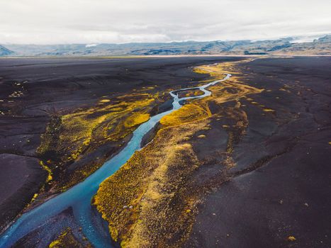 Black volcanic sand beaches in Iceland, a view towards the mainland with a river running trough and some yellow foliage around the water.