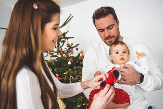 Happy young cheerful caucasian family of three mom dad and baby girl having fun decorating the Christmas tree. Family Christmas portrait.