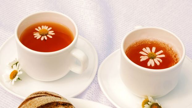 A close-up, a white plate with pastries, biscuits and cookies, decorated with white daisies. On white saucers there are two white cups with chamomile tea. High quality photo