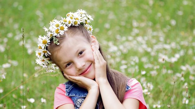 On a chamomile lawn, a sweet girl in a wreath of daisies, smiling, pressing her hands to her cheeks. High quality photo