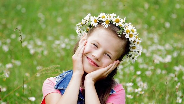 On a chamomile lawn, a sweet girl in a wreath of daisies, smiling, pressing her hands to her cheeks. High quality photo