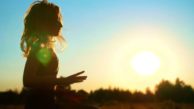 Figure, outline of a beautiful, athletic girl with long blond hair, does exercises, boxing, flying legs, jumping at sunset, against the blue sky, in the sunlight, in summer. High quality photo