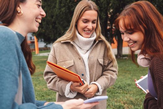 Group of three cheerful female collage students outside their dorm on a cold autumn day, walking on campus to get to their class.