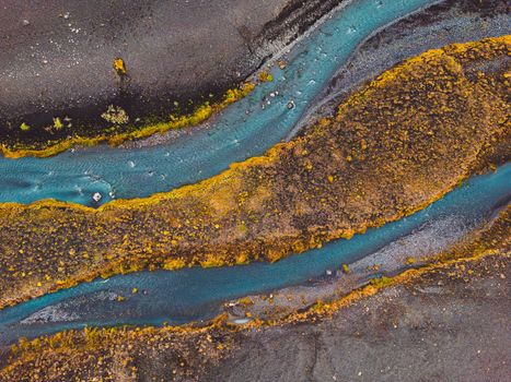 Black volcanic sand beaches in Iceland, a view towards the mainland with a river running trough and some yellow foliage around the water.