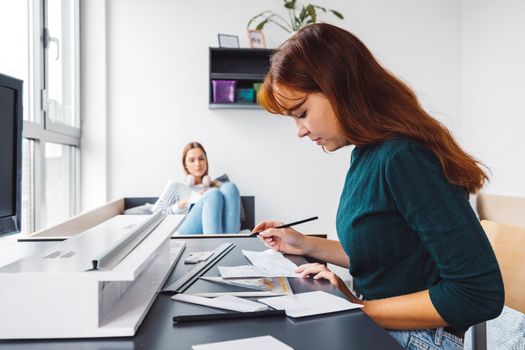 Two young caucasian women, college students studying together in their dorm room in a bright modern room. 