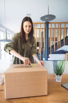 Young caucasian woman receiving a big box of her online orders. Woman opening the package, getting excited to see the stuff she bought. High quality photo