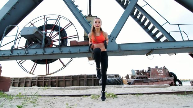 Beautiful athletic woman exercising her muscles . At dawn, near a cargo crane, on the sandy quarry beachHigh quality photo