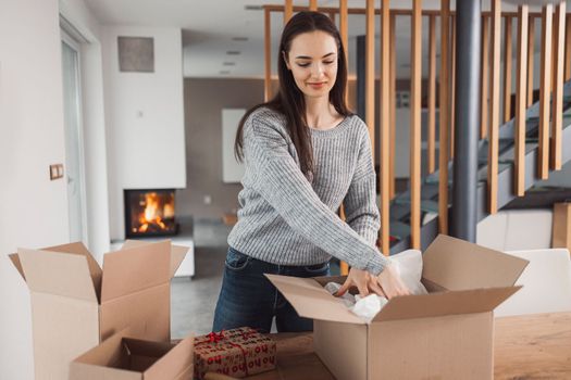 Young caucasian woman wrapping a gift, getting it ready to send in the post. Woman packaging a surprise gift for a family member, packaging it into a brown cardboard box.