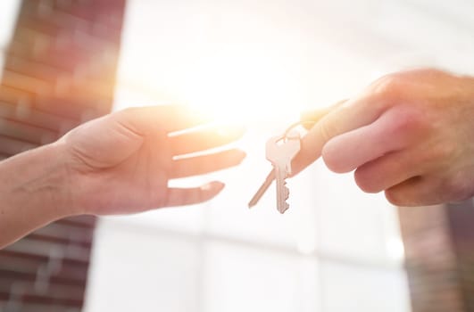 Female hand giving keys from new apartment to male hand on blurred background