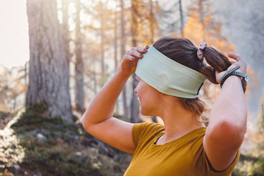 Waist up woman, fall autumn hiker girl outdoor in the forest fixing up her headband.. Happy caucasian woman hiking outdoors. High quality photo