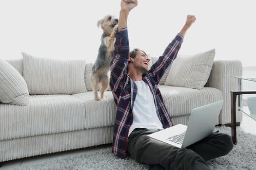 happy guy exults with his dog sitting near the sofa in the living room. the concept of home life