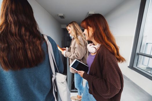 Group of three friends, young caucasian women students walking inside the school during a break, headed to another classroom. Students carrying their books with them. 