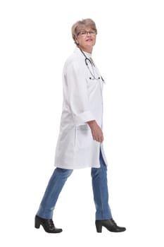 Full length profile studio shot of mature woman doctor in white coat and glasses walking isolated on white background
