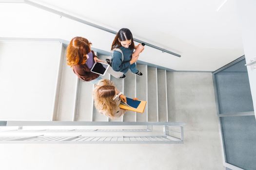 Group of three friends, young caucasian women students walking inside the school during a break, headed to another classroom. Students carrying their books with them. 