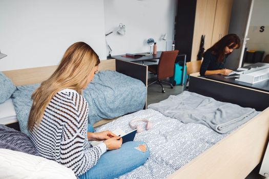 Two young caucasian women, college students studying together in their dorm room in a bright modern room. 