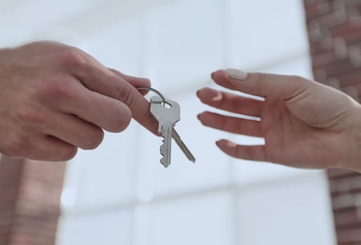 Female hand giving keys from new apartment to male hand on blurred background