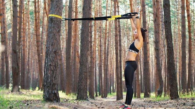 Beautiful, athletic, sexy young woman, coach, instructor, performs exercises, doing exercises. In pine forest, in summer, in sun rays. High quality photo