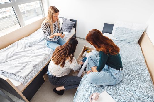 Group of three roommates, college student, young caucasian women, spending time together in their room, studying, talking, having fun, laughing. 