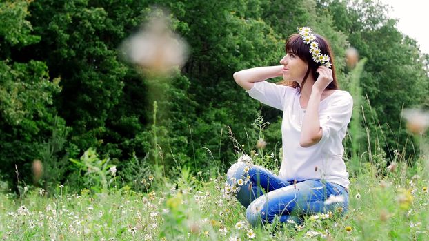 Summer, amidst a chamomile lawn, in a forest, a young woman, a brunette weaves a wreath of chamomiles. High quality photo