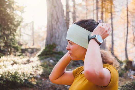 Waist up woman, fall autumn hiker girl outdoor in the forest fixing up her headband.. Happy caucasian woman hiking outdoors. High quality photo