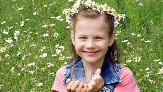 On a chamomile lawn, a sweet girl in a wreath of daisies, smiling, pressing her hands to her cheeks. High quality photo