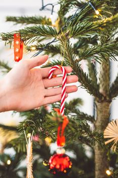 Unrecognizable caucasian woman decorating the Christmas tree, putting red ornament on the tree, holding a red Christmas ornament. 