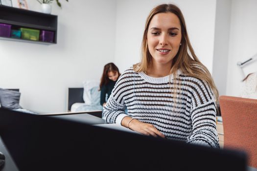 Young caucasian woman, college student studying in her dorm room, sitting by the desk. Bright room with lots of natural light. 