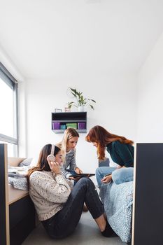 Group of three roommates, college student, young caucasian women, spending time together in their room, studying, talking, having fun, laughing. 