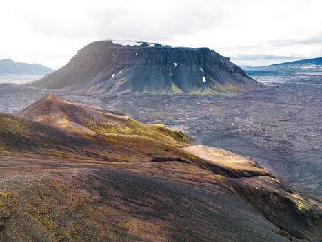 Remote volcanic lands somewhere in Iceland mainland, surrounded by vibrant green bushes and volcanic lands. Volcanic rock formations, small mountains, black grey volcanic rock. No people. 