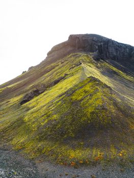 Remote volcanic lands somewhere in Iceland mainland, surrounded by vibrant green bushes and volcanic lands. Volcanic rock formations, small mountains, black grey volcanic rock. No people. 