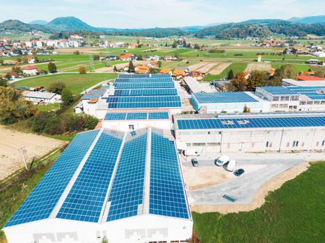 Solar panels installed on a roof of a large industrial building or a warehouse. Industrial building in the country side of Slovenia with residential houses in the background. High quality photo