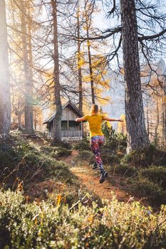 Joyful woman hiker running in the autumn forest, wearing an orange shirt and colorful leggings. Woman jumping in the air while hiking trough the forest. Sunny autumn hike.