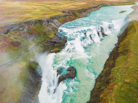 Huge beautiful waterfall Gullfoss, famous landmark in Iceland. River foaming whilst falling down the waterfall, tourist waling by, looking at the waterfall from a view point. High quality photo