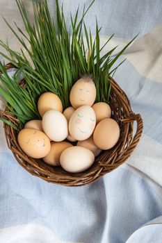 Beautiful painted Easter eggs with a cute face lie in a wooden basket along with fresh green grass