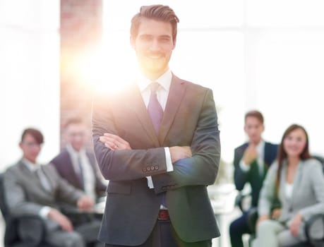 businessman in a suit and tie standing in a modern office building with his arms crossed in front of out team.