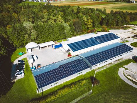 Solar panels installed on a roof of a large industrial building or a warehouse. Industrial building in the country side of Slovenia with residential houses in the background. High quality photo