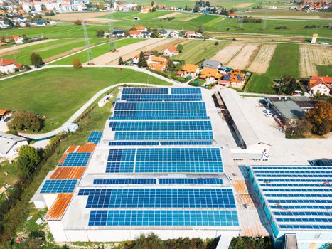 Solar panels installed on a roof of a large industrial building or a warehouse. Industrial building in the country side of Slovenia with residential houses in the background. High quality photo