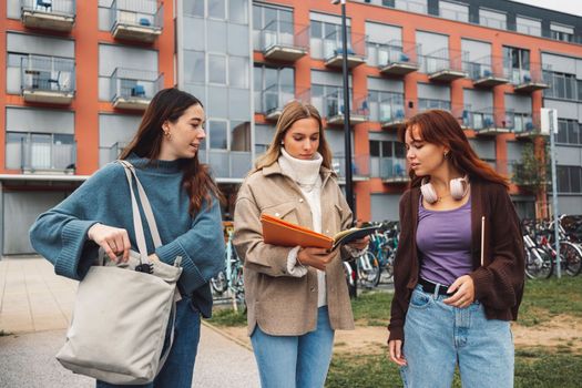 Group of three cheerful female collage students outside their dorm on a cold autumn day, walking on campus to get to their class. 