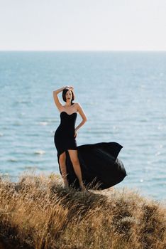 tall girl model in a black dress on the mountain hills near the sea