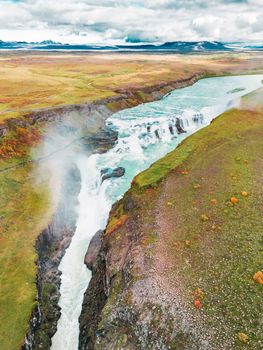 Huge beautiful waterfall Gullfoss, famous landmark in Iceland. River foaming whilst falling down the waterfall, tourist waling by, looking at the waterfall from a view point. High quality photo
