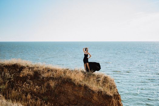 tall girl model in a black dress on the mountain hills near the sea