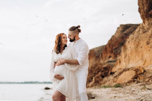 a guy with a girl in white clothes on the seashore next to clay cliffs